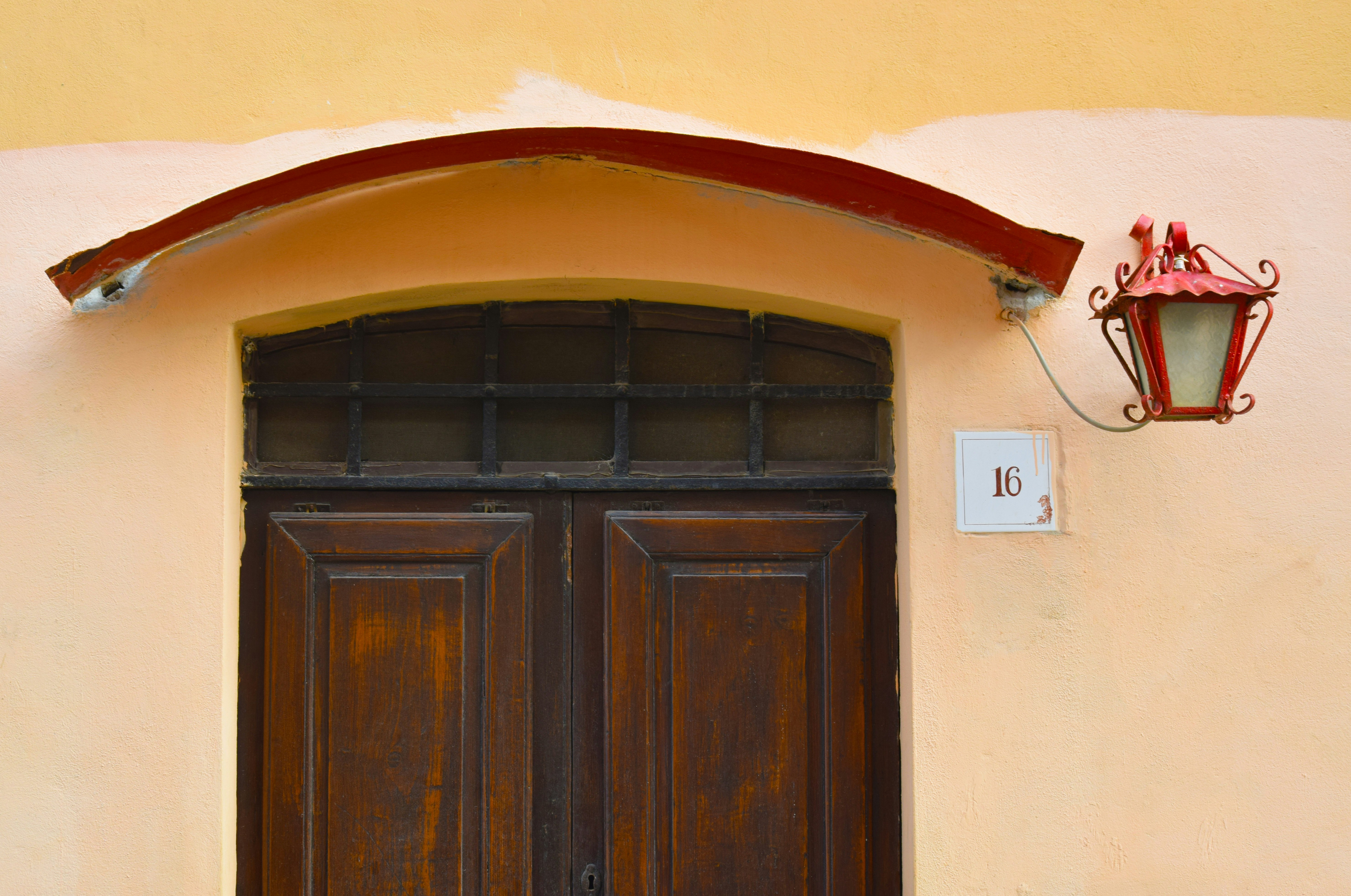 photo of brown wooden panel doors with roof arc and red metal framed post sconce at daytime